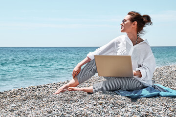 Successful pretty woman using laptop at the beach. Businesswoman working outdoors. Technology and...