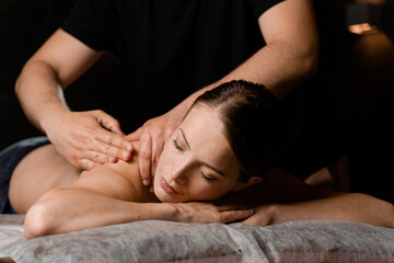 Obraz na płótnie Canvas Attractive girl is relaxing on classic massage procedure in spa. Manual therapy. Masseur is doing shoulder massage.