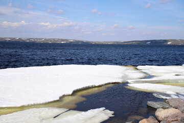 view of the blue lake with melting ice on the hilly shore