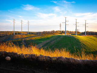 Fototapeta premium Industrial Landscape with Electricity Pylons on the Hills. Dramatic Cloudscape over Electric Poles and Cables on Blue Sky. Retro Technology Backdrop Image with Space for Text or Design