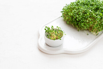 Raw microgreen alfalfa sprouts on a cutting board on a white background.
