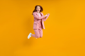 Fototapeta na wymiar Full length photo of funny caucasian lady in pink suit jumping up high see low shopping prices direct finger at side on advert banner, isolated yellow color background in studio