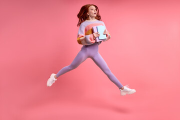 Fototapeta na wymiar Full body profile photo of young caucasian redhead female student jump high holding notebook in hands hurry in university, in casual outfit isolated over pink color background. Portrait