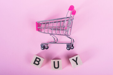BUY- word on wooden cubes, on a pink background with a shopping trolley.