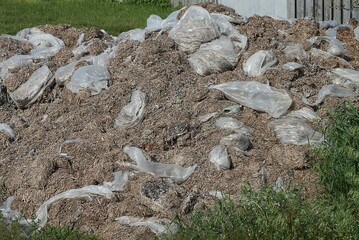 a large pile of brown dry manure with plastic white torn bags outside in the green grass