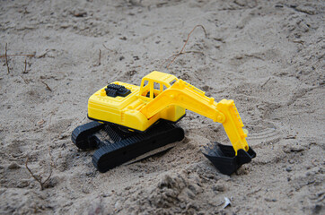 Yellow plastic excavator in the sand. Toy construction equipment. Children's toys on the beach.