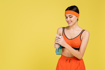 happy woman in orange sportswear opening sports bottle isolated on yellow.