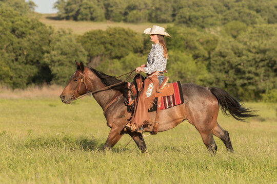 Women galloping a horse in a pasture wearing western attire 