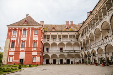 Fototapeta na wymiar Opocno castle, renaissance chateau, courtyard with arcades and red facade, green lawn with statue and flowers in foreground, sunny summer day, aristocratic residence, Czech Republic