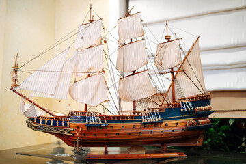Wooden old sail ship model on a stand on a glass table. It has three masts and lateen sails in the...