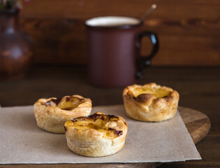 Three small quiches of home cooking on baking paper. A mug in the background, a wooden background. Selective focus.