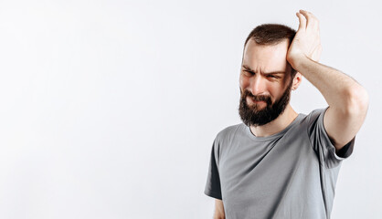 Naklejka premium Portrait of handsome young man frowning while holding hands near head on white background with space for advertising mock up