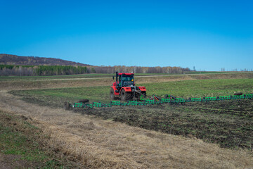 Fototapeta premium The red tractor is working the soil before planting.