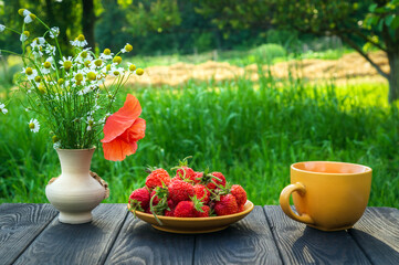 Fototapeta na wymiar Summer still life of a plate with strawberries and coffee on a table with flowers. Summer morning or evening background