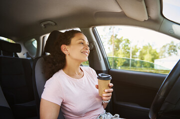 Young African ethnicity woman enjoying coffee break in her car during stop