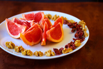 Wonderful vegan food: grapefruit sliced with slices, walnut kernels, dried cranberries stand on a white plate