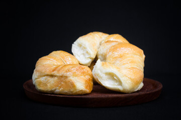 2 croissants in a syrup bath, one on top of the other, on a wooden plate. Black background