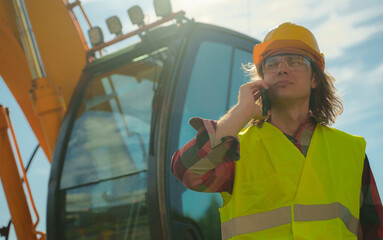 Excavator operator in hard hat talking by smartphone.
