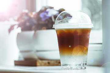 A cold, double-layer espresso tonic in a plastic glass sits on a windowsill in a coffee shop.