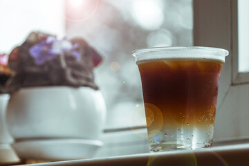 A cold espresso tonic in a plastic glass sits on a windowsill in a coffee shop. Vertical photo.