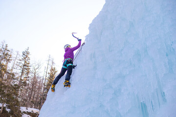 Female ice climber silhouette swinging ice axes on her way up vertical ice waterfall, side view