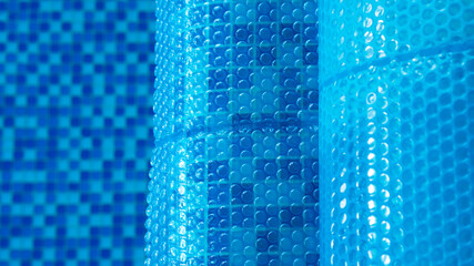 Blue tarpaulin pool cover. Bubble awning wrap for swimming pool cover. Swimming pool with a blue water. Close up. Top view. Selective focus. - obrazy, fototapety, plakaty