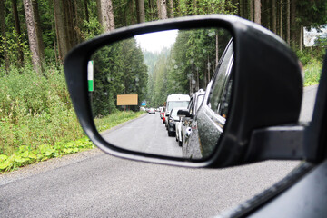 Car side mirror with traffic jam on a road in a forest