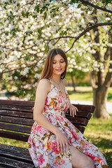 Naklejka premium A girl like from a fairy tale sits barefoot on a bench in a green park