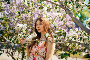 Cute girl in a bright dress soit in blooming gardens of apple and lilac trees
