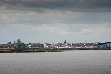 Fototapeta na wymiar Galway Cathedral and The Long walk colorful houses. Cloudy sky. View from the ocean. Town famous landmark.