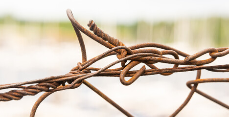 Rusted and twisted metal wire fence on white and green background with shallow focus, for...