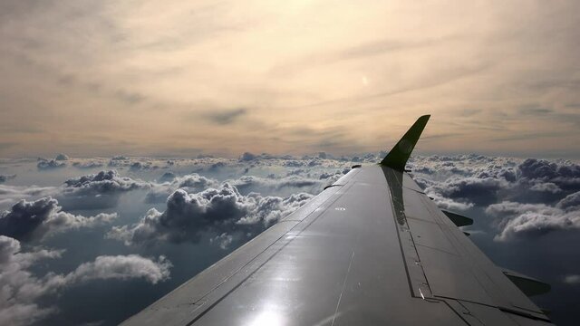 Wing filmed from the airplane which is flying over clouds on dawn. A view from the moving jet on skyline. There is an aerial landscape during dusk. Concept of travelling by air vehicles. Voyage theme.