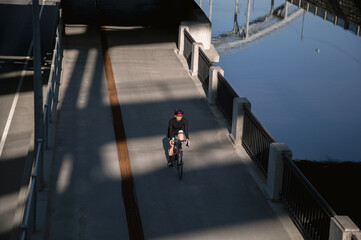 A woman rides a bicycle along the embankment in the morning illuminated by the sun. Outdoor sports. Sports ammunition.