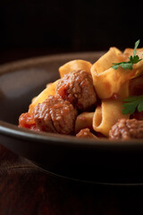 Pappardelle pasta with tomato sauce and meatballs. Dark background. Close up. 