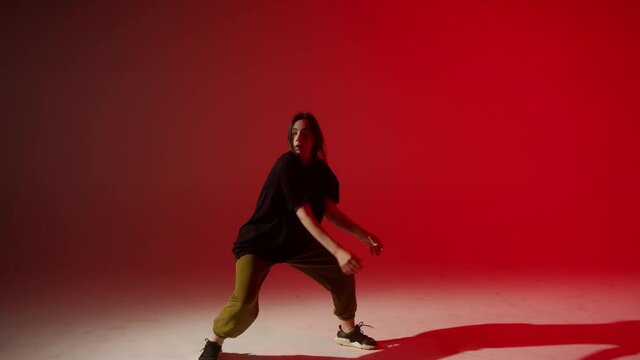 Young woman wearing black T-shirt dancing contemporary on red neon background in studio. Shooting of modern slow dance choreography. Motion of female dancer expressing feelings in dance movings. 