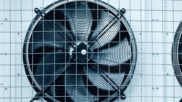 Industrial refrigeration unit mounted on wall of warehouse building. Unit with external cooling fans. Rotating blades. Metal turbine. Air conditioning equipment. Protective steel grill. Freezer unit