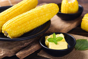 Sweetcorn cob and butter in a bowl on wooden background