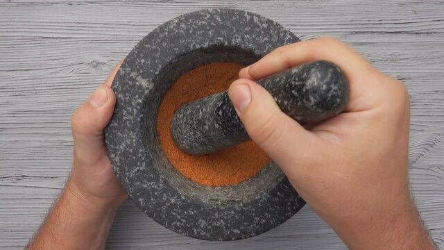 Top view of a pestle mixing finely grounded spices in the grey stone mortar