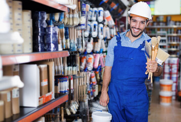 Positive builder standing with paint and brushes satisfied with purchases in paint shop.