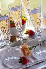 Tilted view of crystal flute glasses filled with rose wine and a bowl of strawberries in behind.