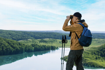Obraz premium Hiker man looking in binoculars on the mountain. Hiking active people lifestyle.