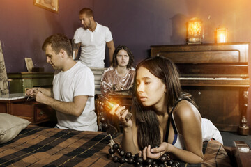 Group of young adults inspecting wooden rosary, trying to find solution of conundrum in escape room...