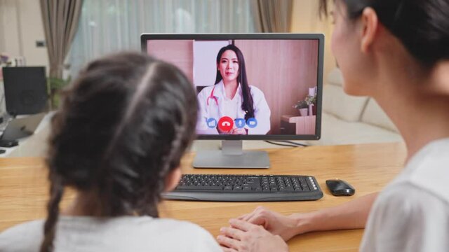 Asian mom and daughter virtual video call with doctor in living room.	

