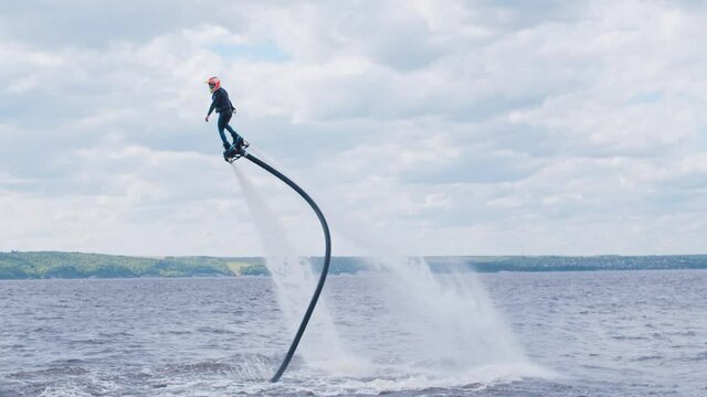 Sportive man flying above the water on a flyboard with a waverunner nearby