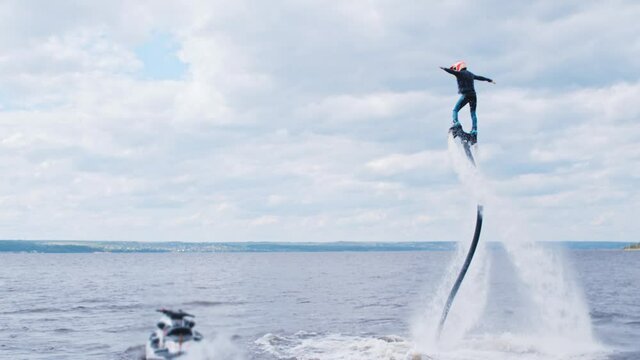 Sportive man flying above the river on a flyboard with a jet ski nearby