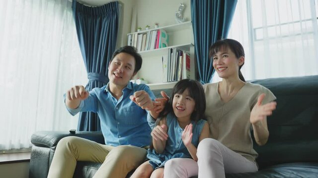 Asian family, Parent and kid sit on sofa watch TV and dance in house.