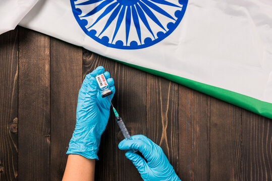 Hands of doctor wearing gloves holding coronavirus (COVID-19) vial vaccine and syringe with flag India on wooden background, India Vaccination