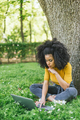 Beautiful afro woman typing on a laptop in a garden.