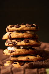 PRIMER PLANO DE GALLETAS UNA SOBRE OTRA CON CHIP DE CHOCOLATE Y MASMELLOS EN UNA MESA NEGRA  CON UNA TELA 