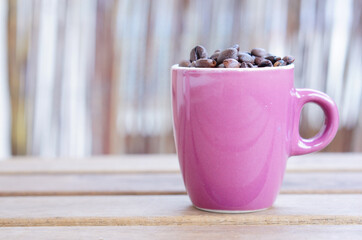 Closeup of a ceramic pink cup filled with coffee beans on wooden planks with copy space beside it